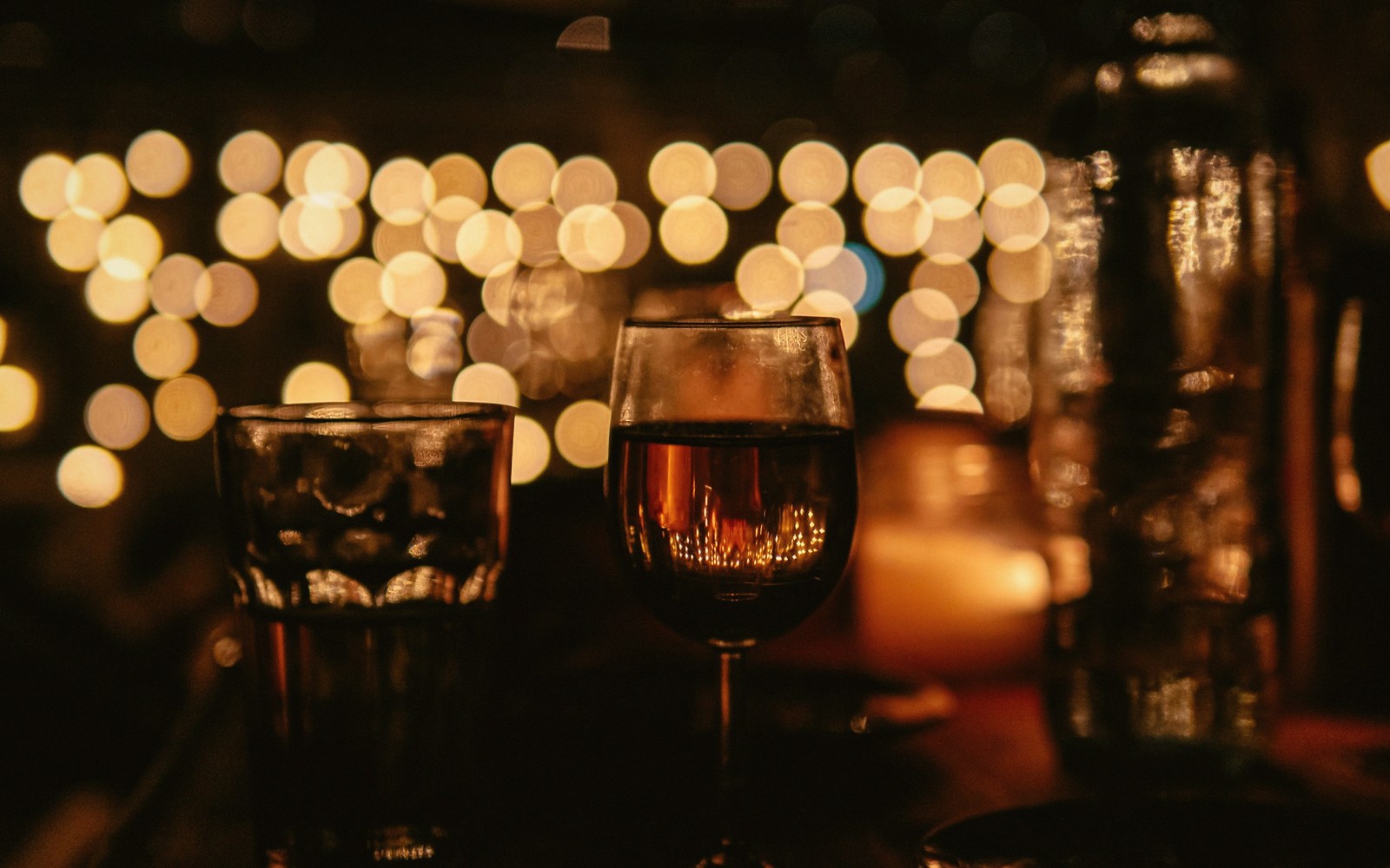 Wine glass and tumbler on a bar table lit by string lights and a candle